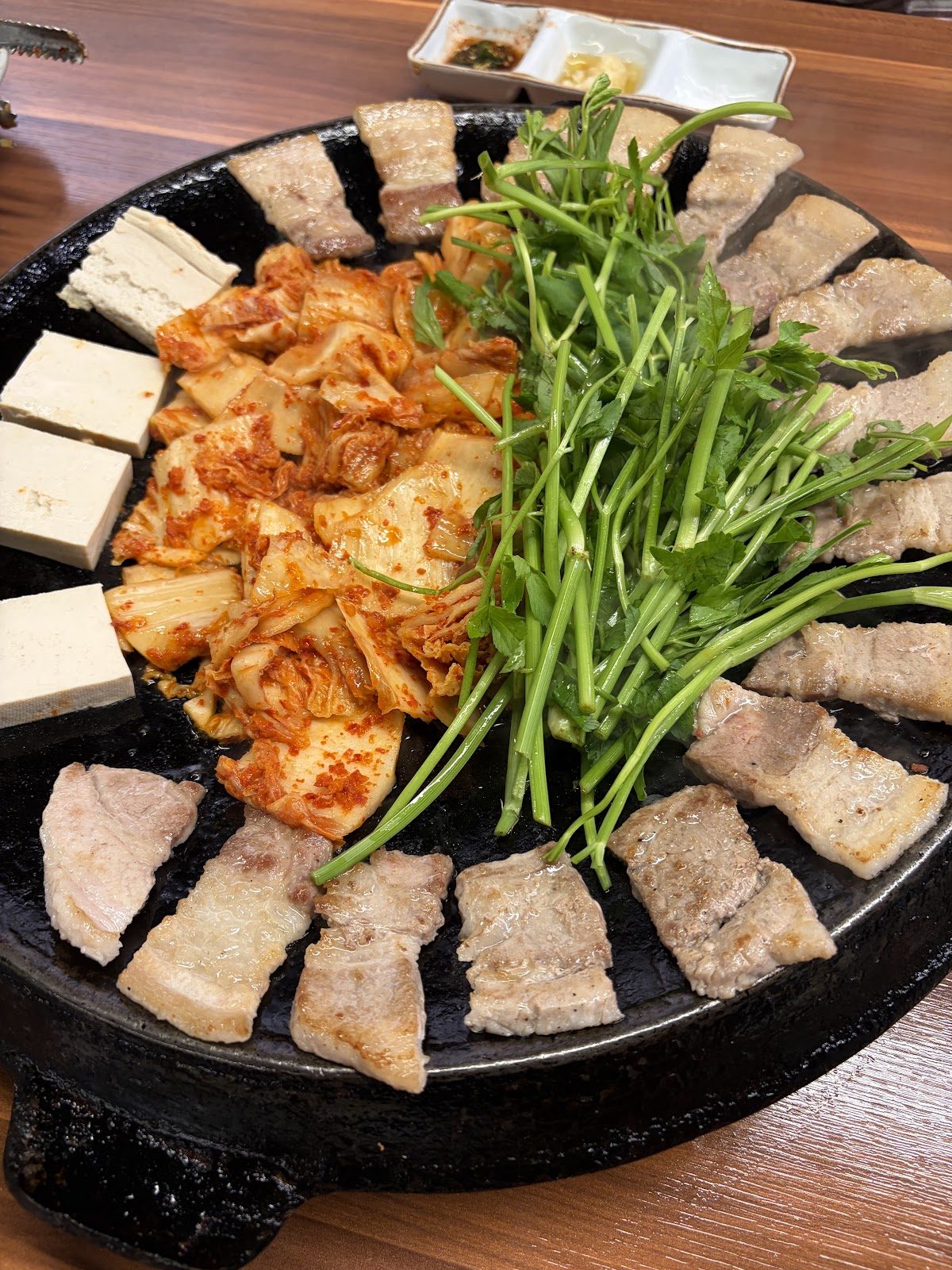무쇠 불판 위 삼겹살과 볶은 김치에 생미나리를 한 줌 올린 모습
