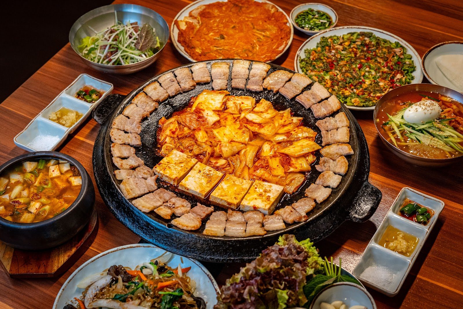 무쇠 불판에 삼겹살을 둘러 굽고 가운데에 볶은 김치와 두부를 올린 한상 — 무쇠김치삼겹 명동점