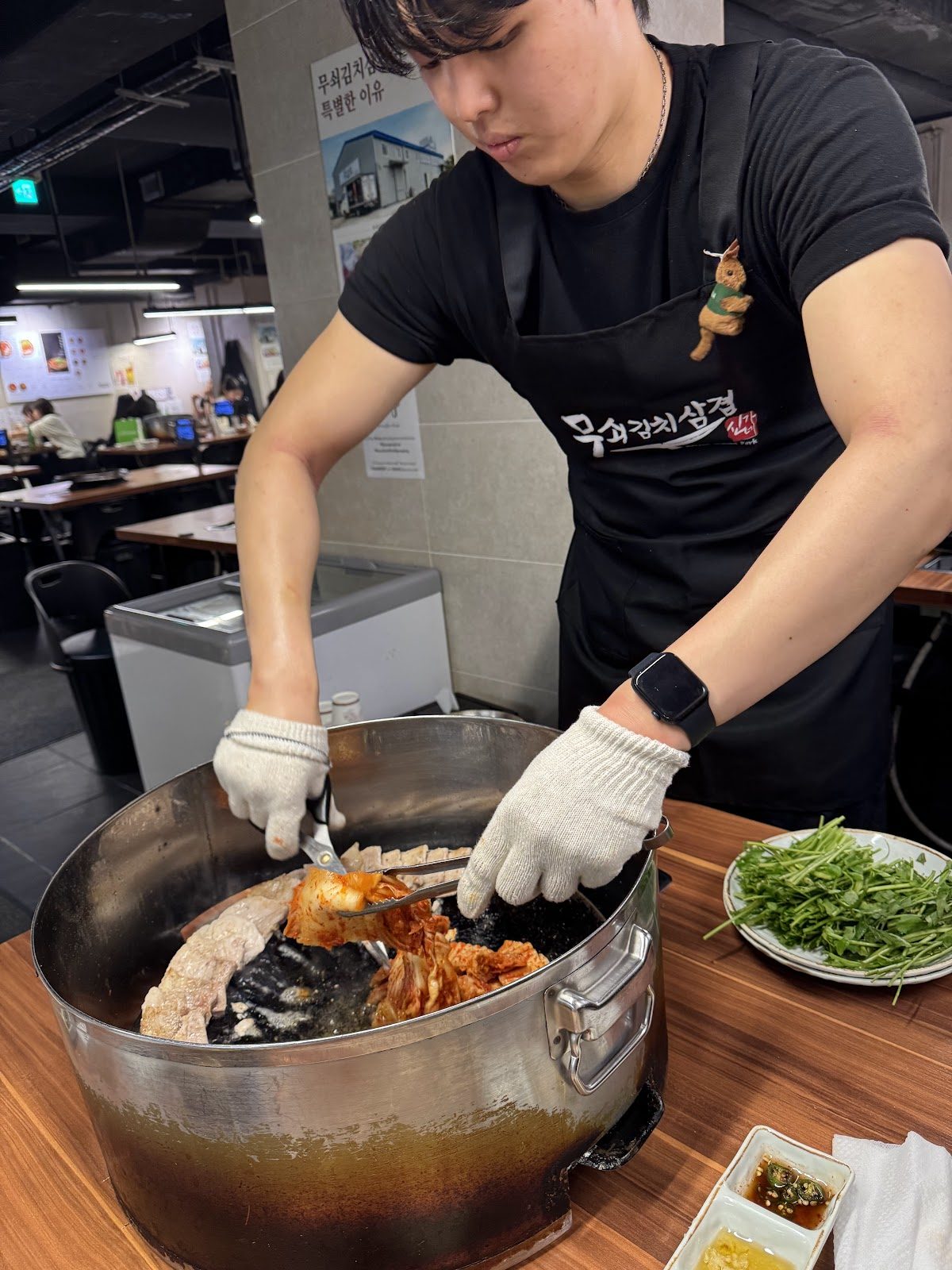 검은 앞치마를 입은 직원이 가위로 불판 위 고기를 잘라 주는 모습